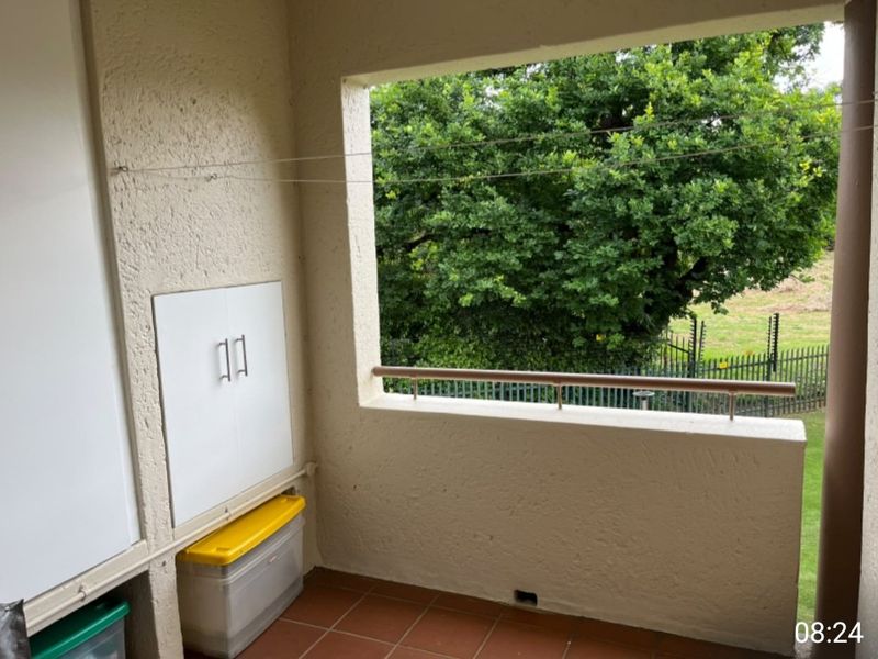 A covered balcony featuring tiled flooring, a built-in storage cupboard, and a metal balustrade overlooking a garden area.