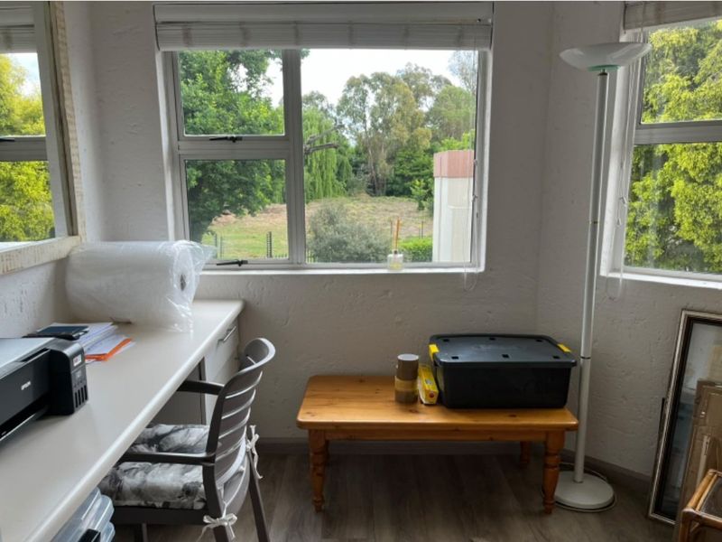 A functional home office space featuring a built-in desk, laminate flooring, and large windows providing natural light and garden views.