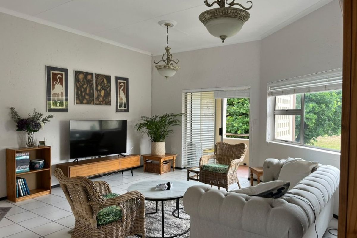 A bright living room featuring tiled flooring, coved ceilings, and a sliding glass door providing access to an outdoor patio area.
