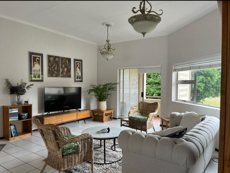 A bright living room featuring tiled flooring, coved ceilings, and a sliding glass door providing access to an outdoor patio area.