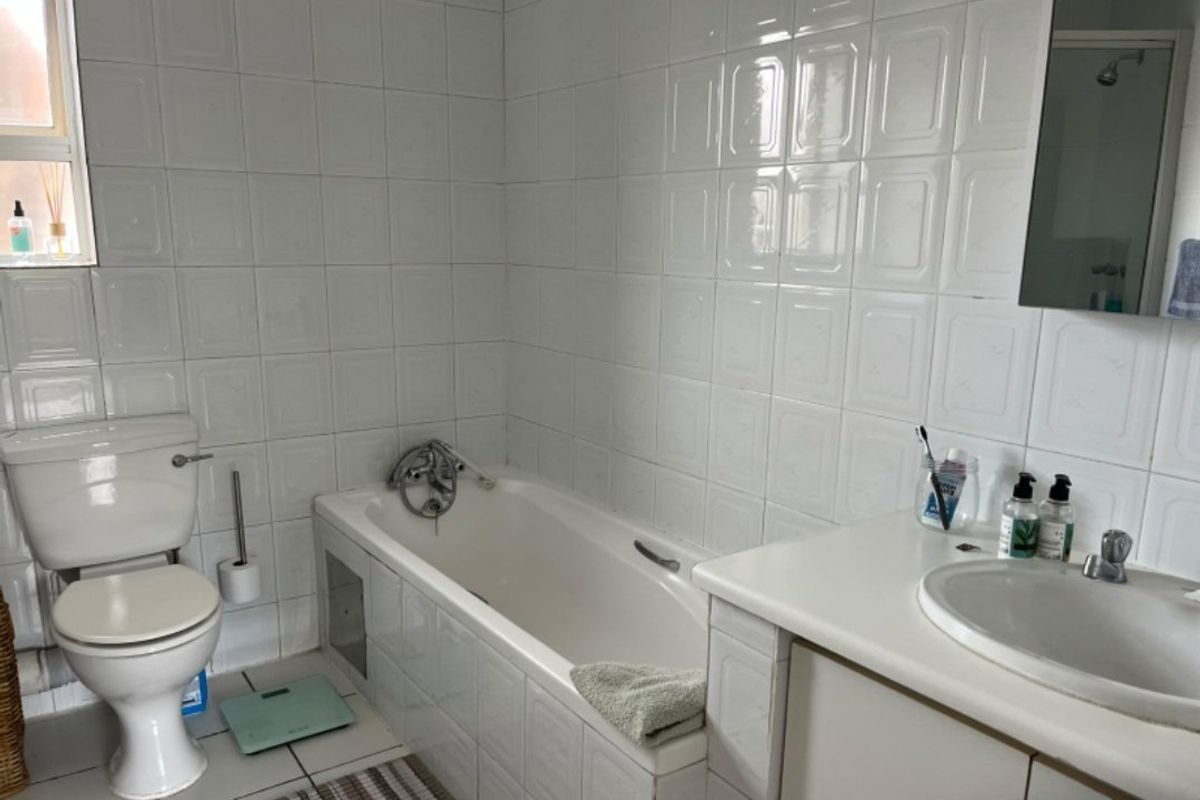 A functional bathroom featuring a built-in bathtub, vanity cabinet with integrated basin, and full-height wall tiling.
