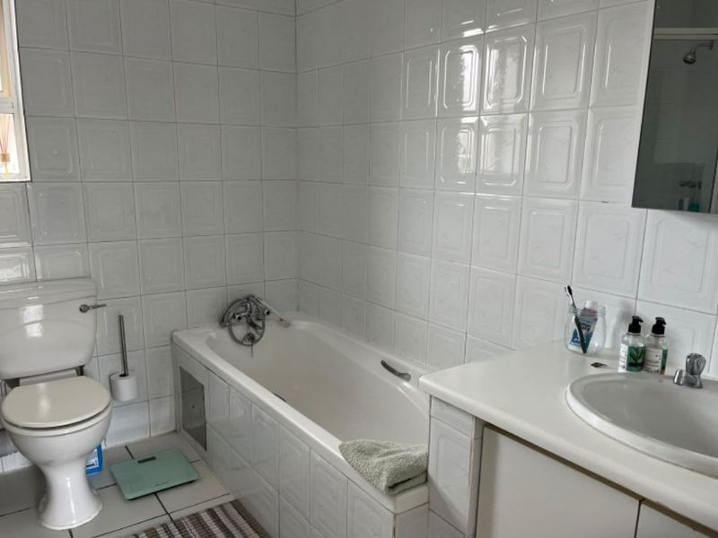 A functional bathroom featuring a built-in bathtub, vanity cabinet with integrated basin, and full-height wall tiling.