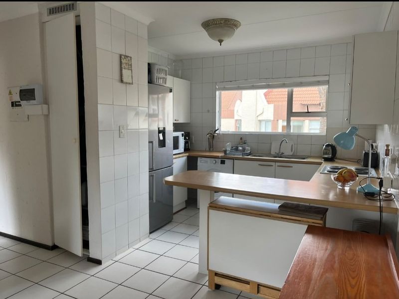 A functional kitchen featuring tiled flooring, white cabinetry, laminate countertops, and a built-in hob, offering a practical layout with ample storage space.