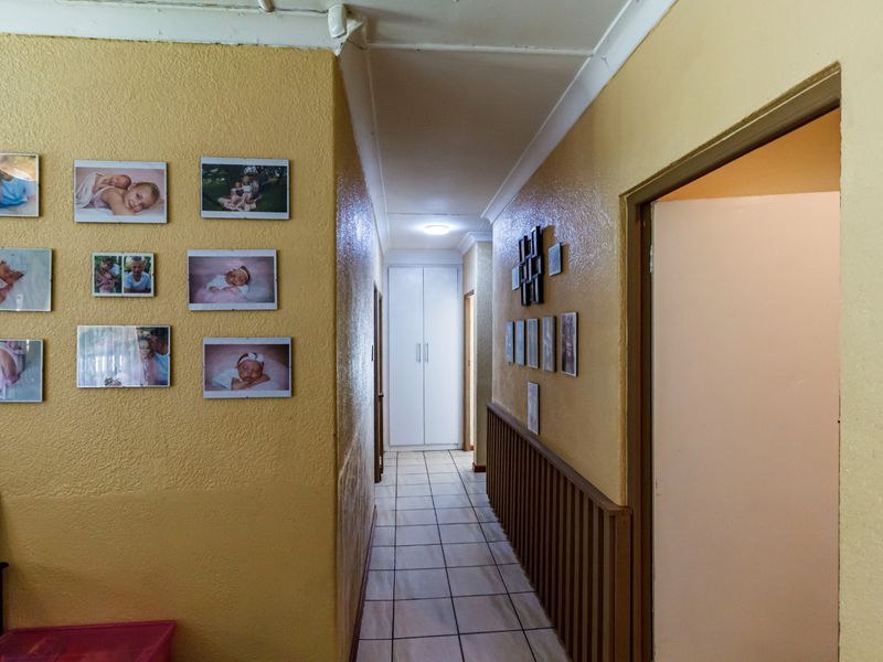 A functional hallway featuring tiled flooring, a built-in storage cupboard, and a timber balustrade, providing access to various rooms within the home.