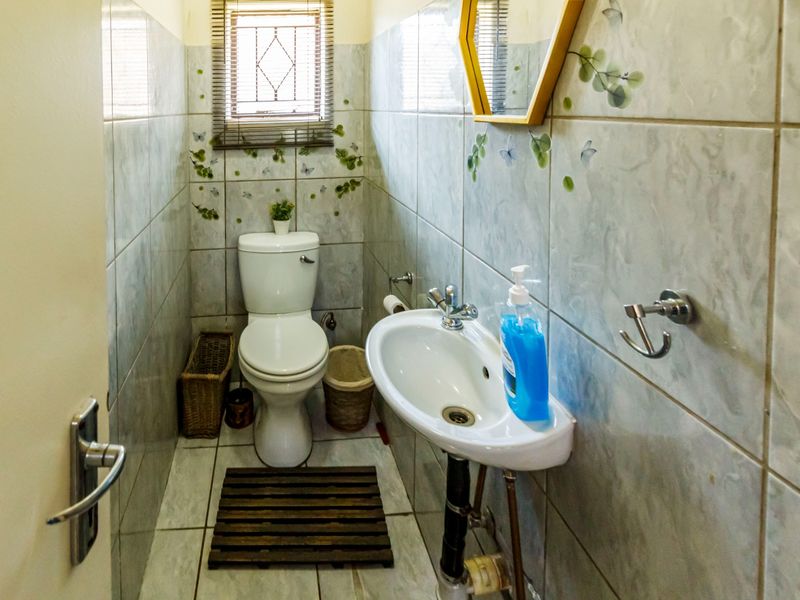 Compact guest bathroom featuring tiled walls and flooring, a wall-mounted basin, and a standard toilet.