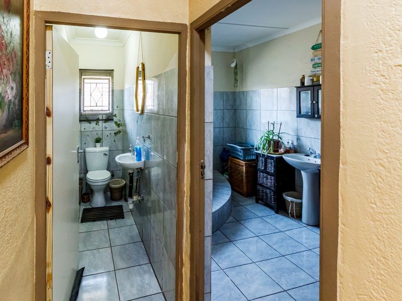 A view through doorways into two adjacent bathrooms featuring tiled walls, ceramic flooring, pedestal sinks, and a toilet.