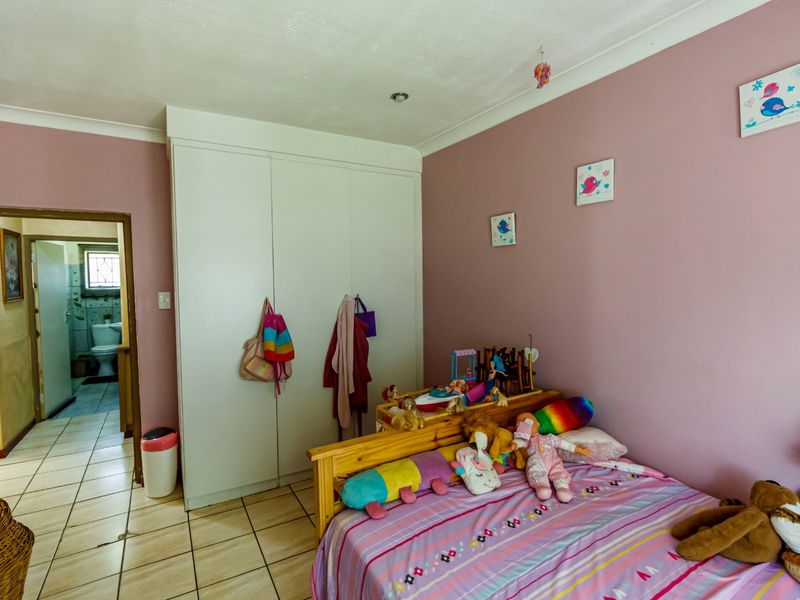 A bedroom featuring built-in wardrobes, tiled flooring, and recessed lighting, with an adjoining view into a bathroom area.