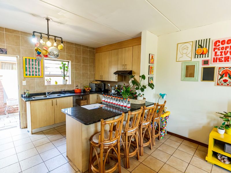 A functional kitchen featuring light wood cabinetry, granite countertops, a breakfast bar, and tiled flooring with direct access to an outdoor area.