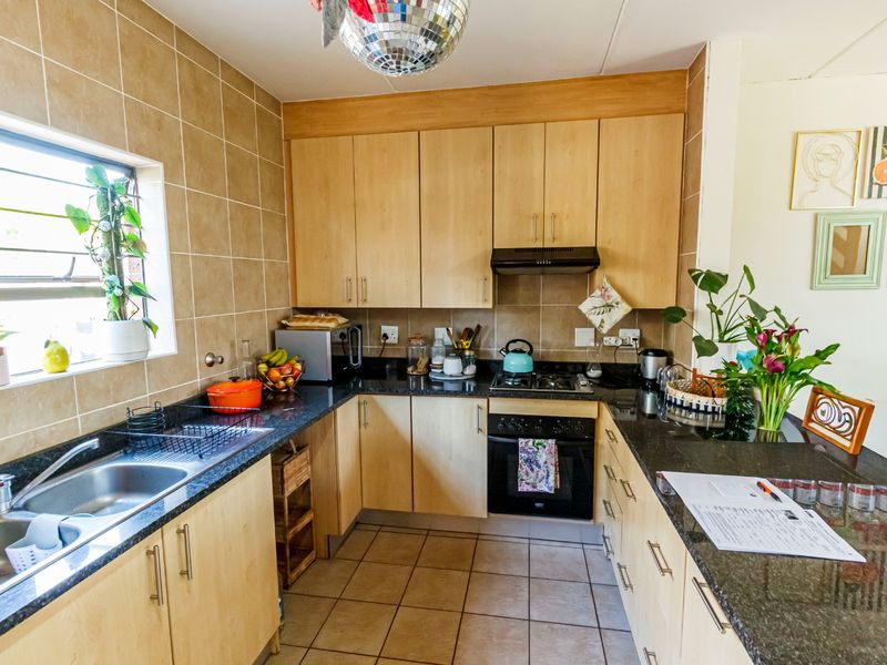 A functional kitchen featuring light wood cabinetry, granite countertops, a built-in oven with hob, and tiled finishes throughout.