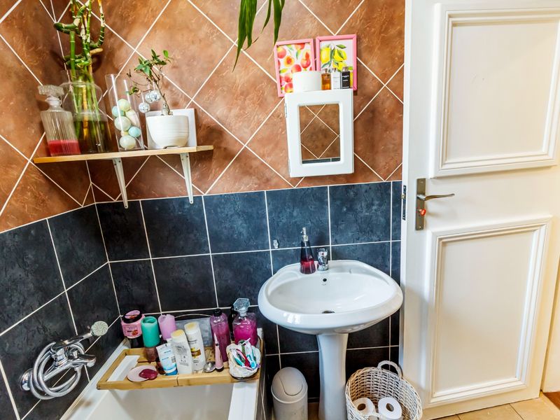 A functional bathroom featuring a pedestal basin, bathtub with shower mixer, and contrasting tiled wall finishes.