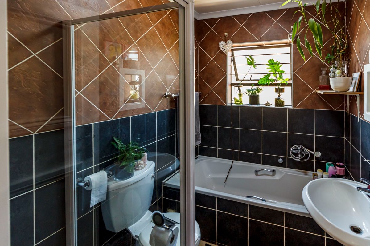 A functional bathroom featuring a built-in bathtub, wall-mounted basin, toilet, and a separate shower enclosure with contrasting dark and brown tiled wall finishes.
