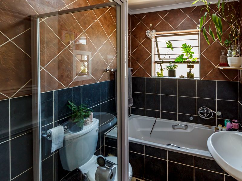 A functional bathroom featuring a built-in bathtub, wall-mounted basin, toilet, and a separate shower enclosure with contrasting dark and brown tiled wall finishes.