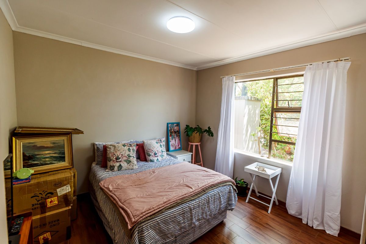 A bedroom featuring laminate flooring, neutral wall tones, and a large window allowing natural light, providing a comfortable and functional living space.