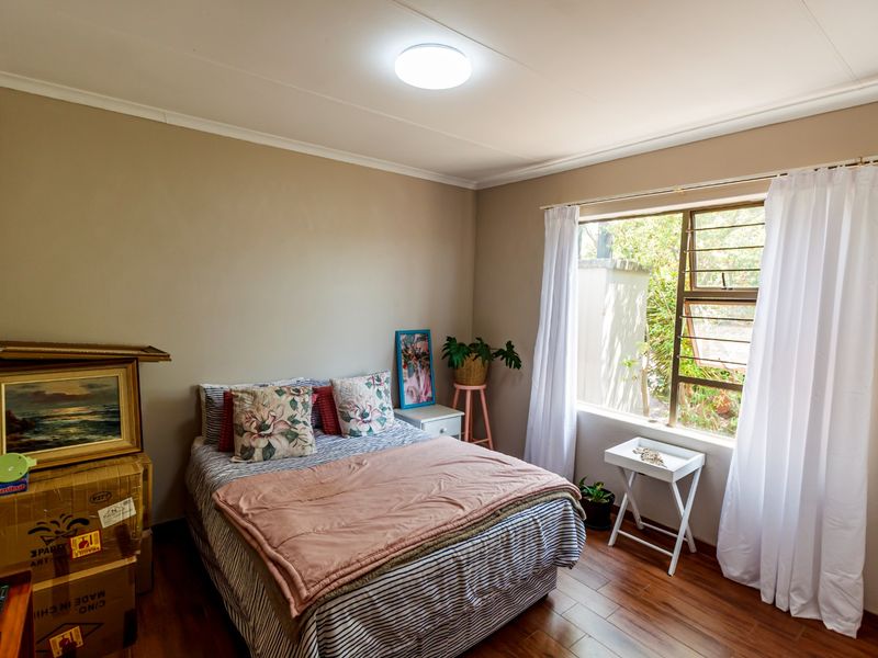 A bedroom featuring laminate flooring, neutral wall tones, and a large window allowing natural light, providing a comfortable and functional living space.