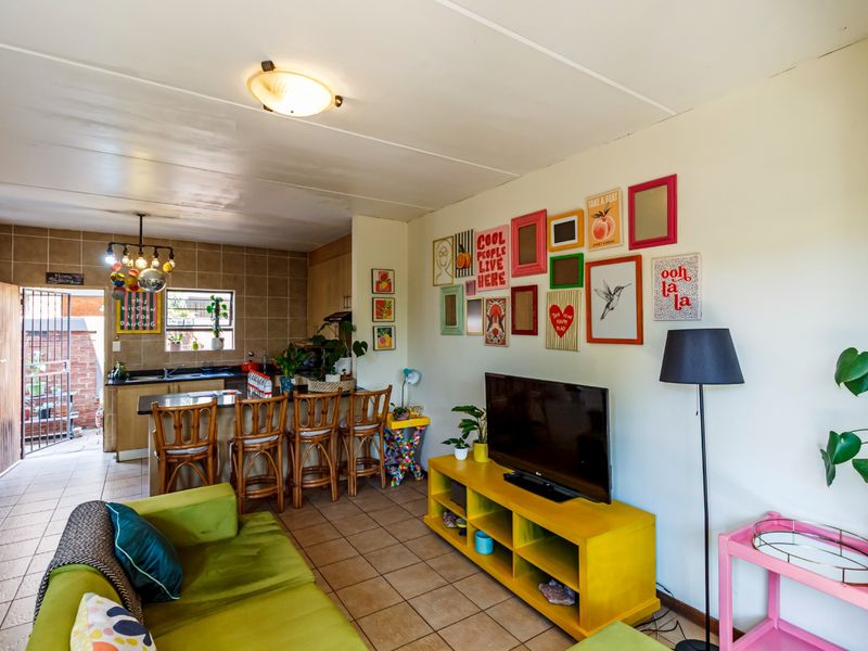 An open-plan living and kitchen area featuring tiled flooring, a breakfast bar, and a functional kitchen layout with tiled backsplash.