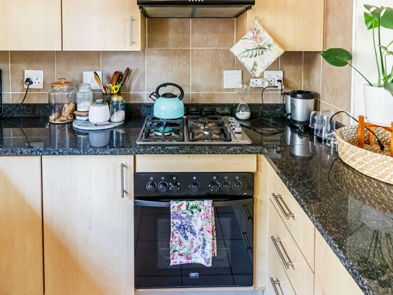 A functional kitchen featuring light wood cabinetry, dark granite countertops, a gas hob, built-in oven, and a tiled backsplash.