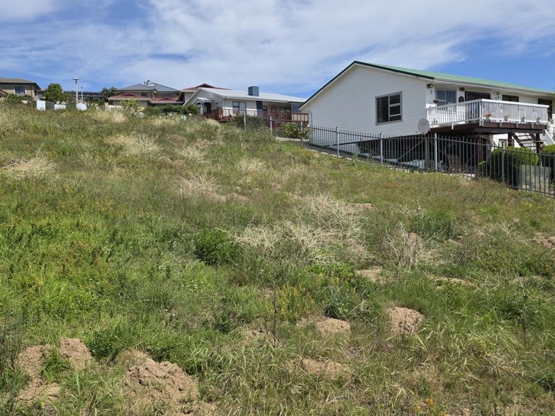 A sloped residential vacant land plot featuring natural grass cover and metal perimeter fencing, situated in an established neighborhood.