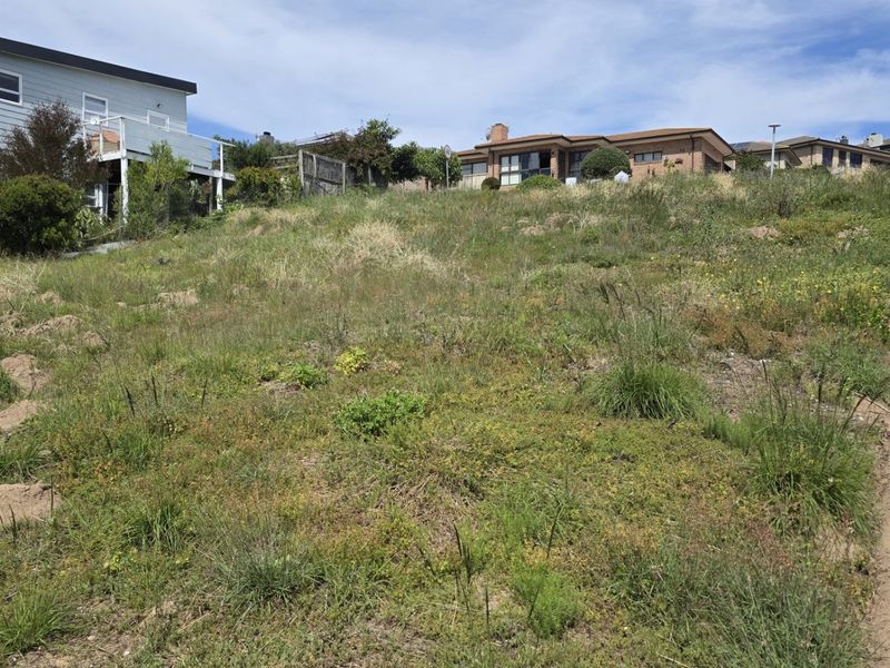 A sloped, undeveloped residential land parcel featuring natural grass coverage and perimeter fencing, situated in an established neighborhood setting.