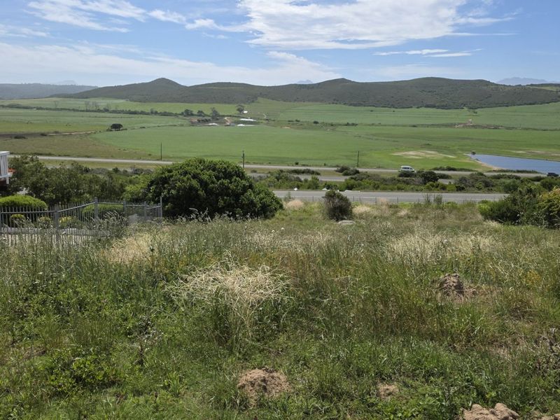 A scenic view overlooking open grassland, rolling hills, and a distant water body from the residential property.