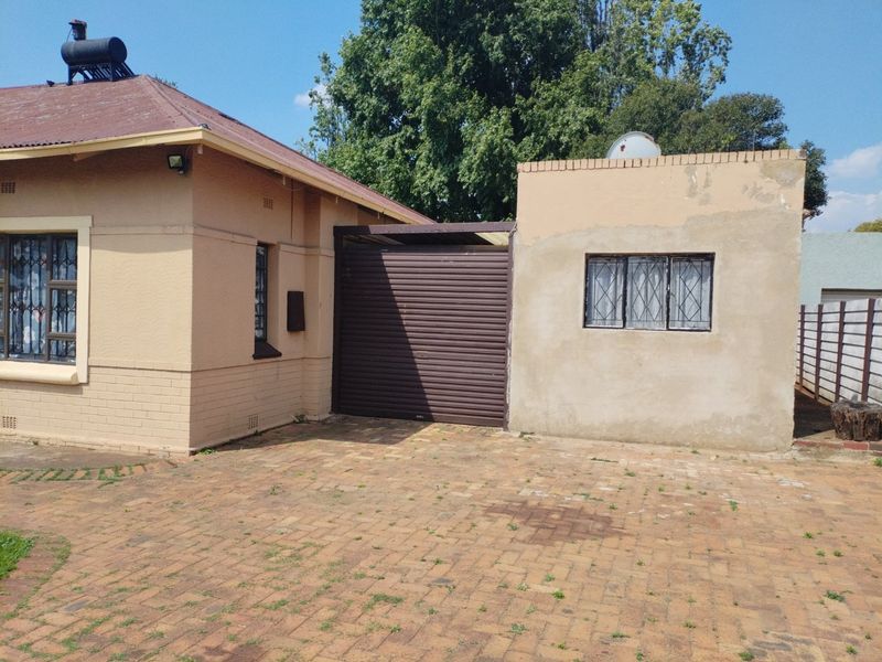 Exterior view of the property featuring a brick driveway, security bars on windows, and a roller shutter door entrance.