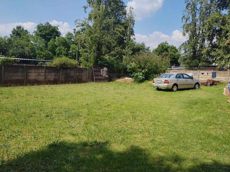 A spacious backyard area featuring a large lawn, enclosed by a precast concrete boundary wall with integrated electric fencing.