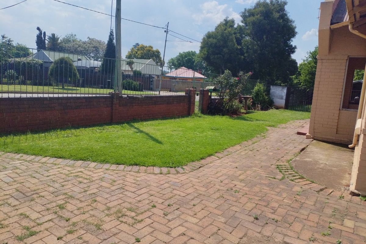 A rear garden area featuring brick paving, a lawn, and a brick boundary wall with metal security fencing.