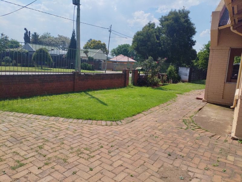 A rear garden area featuring brick paving, a lawn, and a brick boundary wall with metal security fencing.