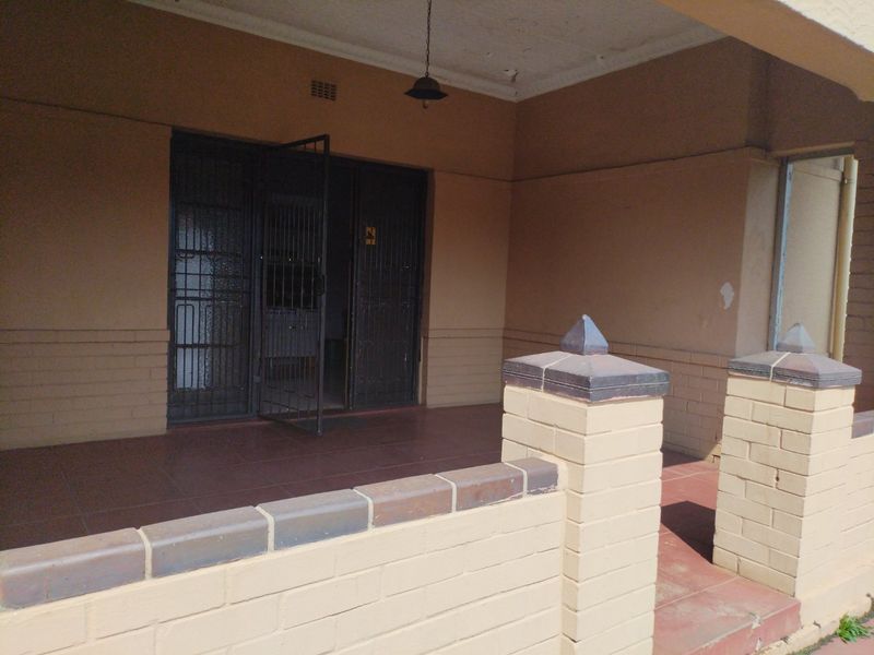 A covered patio area featuring tiled flooring, a low brick boundary wall, and a secure metal entrance gate.