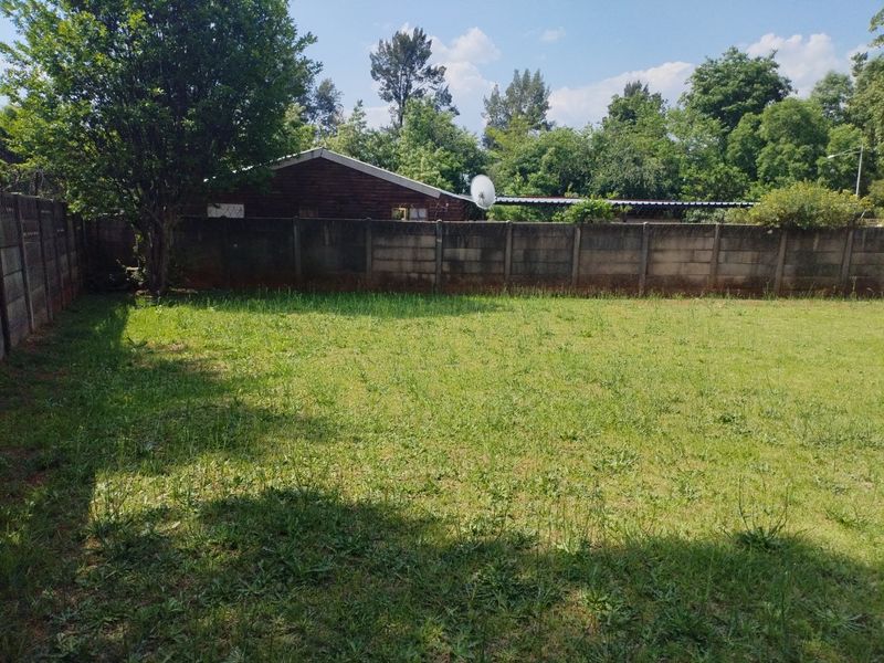 A spacious, level backyard featuring a large lawn area enclosed by precast concrete boundary walls.