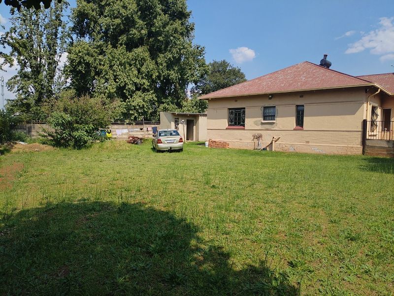 Rear view of the property featuring a large garden, brick exterior walls, and a corrugated metal roof with a solar geyser.