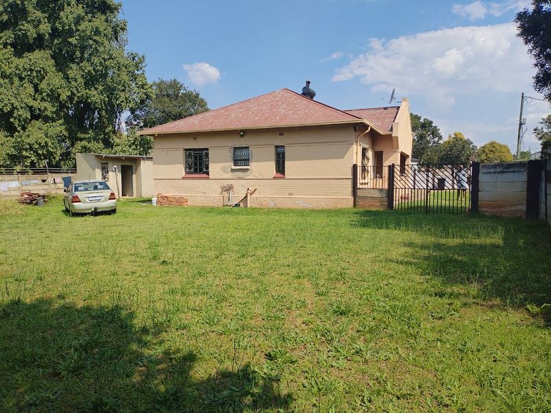 Rear view of a single-story house featuring a corrugated metal roof, security bars on windows, and a large backyard with perimeter walling.