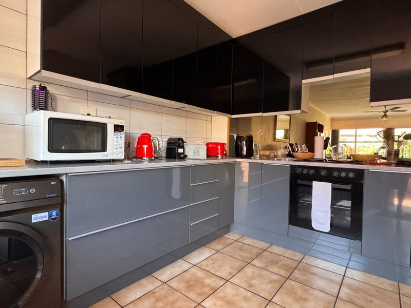 Modern kitchen featuring high-gloss grey and black cabinetry, integrated oven, hob, and tiled flooring with a functional layout.