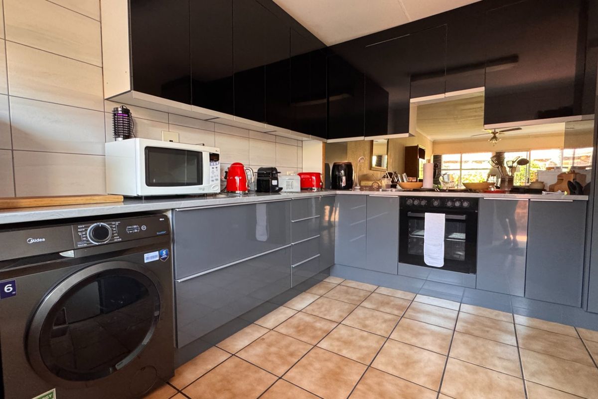 Modern kitchen featuring sleek grey and black cabinetry, built-in oven, hob, and tiled flooring with a functional layout.