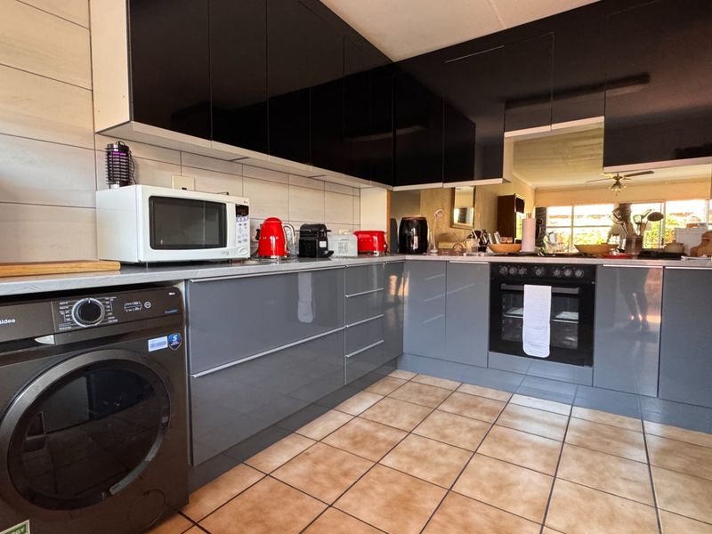 Modern kitchen featuring sleek grey and black cabinetry, built-in oven, hob, and tiled flooring with a functional layout.