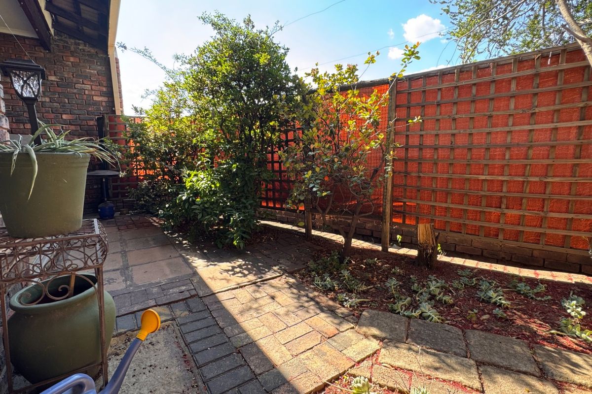 A private rear courtyard featuring brick paving, established garden beds, and trellis fencing, providing a quiet outdoor space.