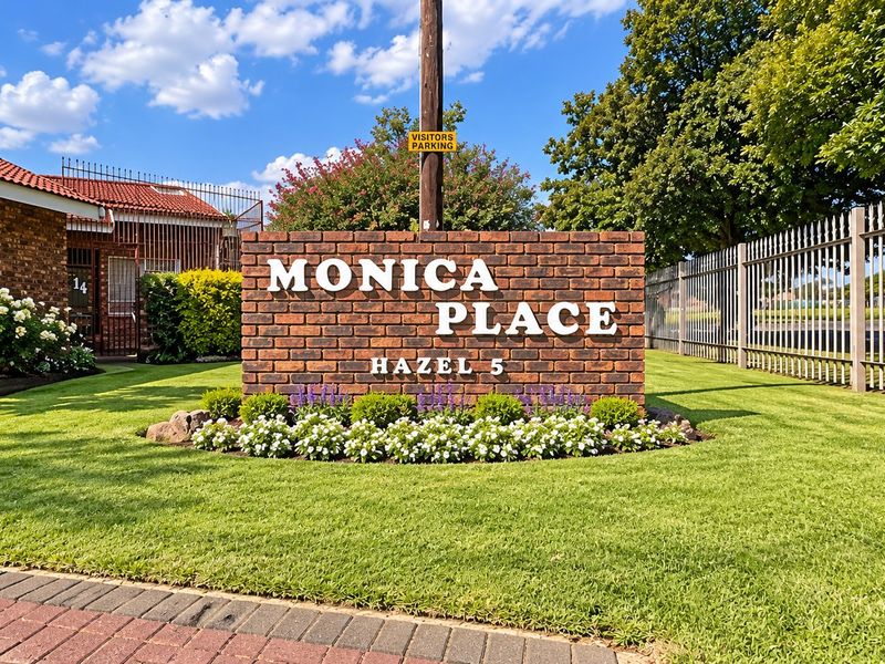 Entrance view of Monica Place townhouse complex featuring a brick signage wall, manicured garden, and secure metal perimeter fencing.