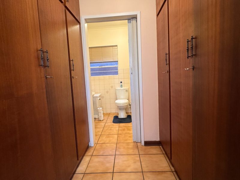 A hallway featuring extensive built-in wooden cabinetry and tiled flooring, leading directly into a bathroom area.
