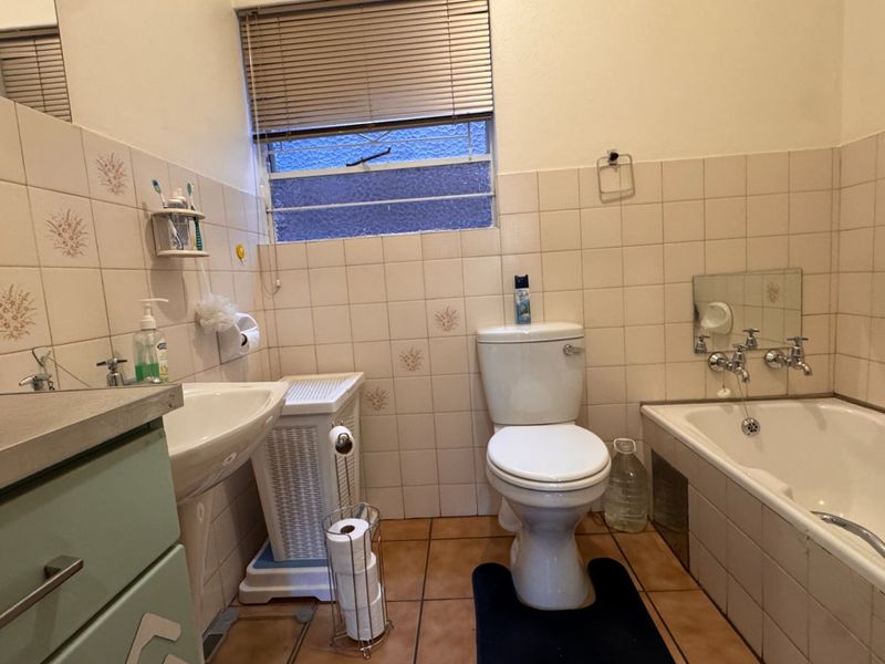 A dated bathroom featuring a pedestal sink, toilet, and bathtub with tiled walls and flooring, requiring cosmetic updates to modernize the space.