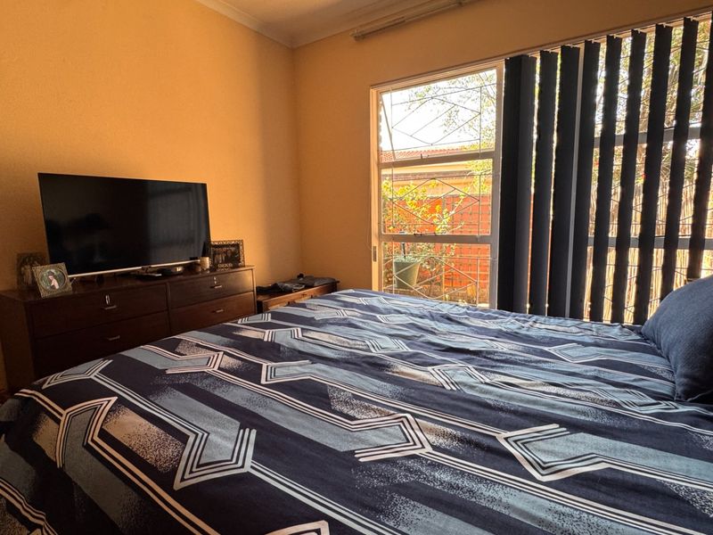 A bedroom featuring a large sliding window with vertical blinds, providing natural light and a view of the exterior.