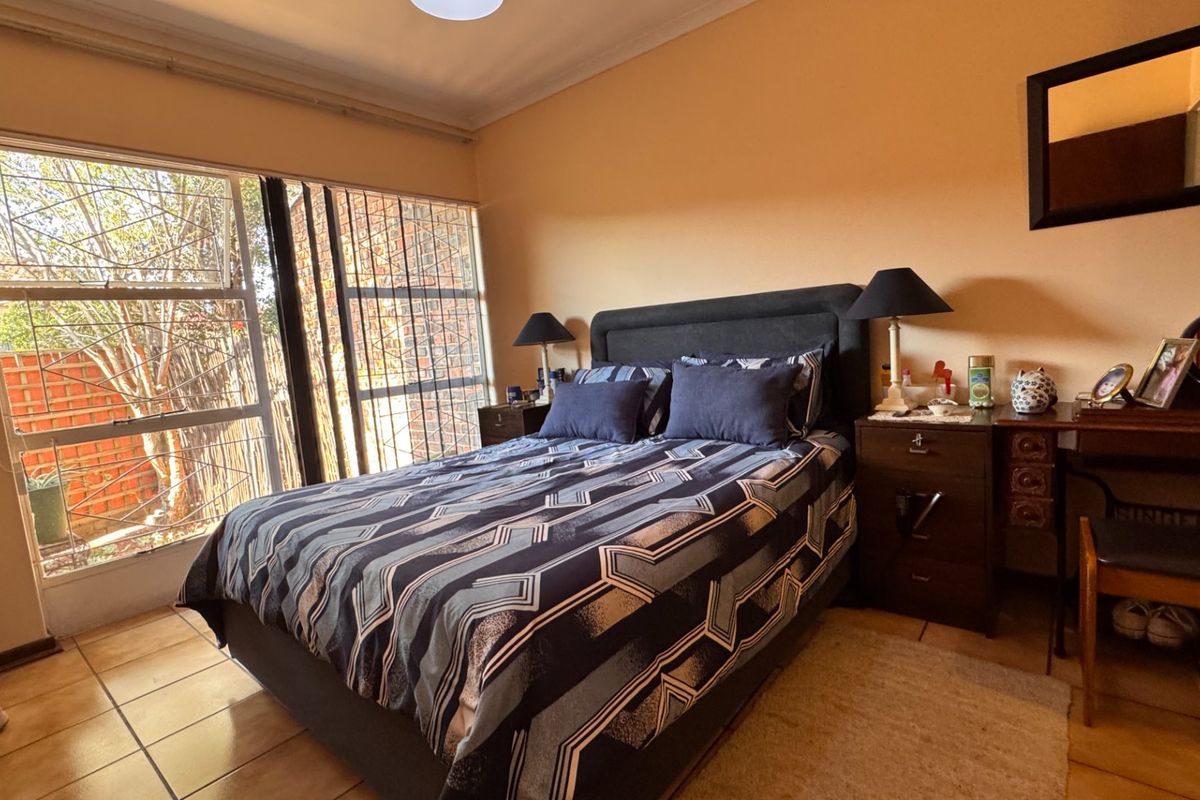 A bedroom featuring tiled flooring and a large window with security bars, providing natural light and a view of the exterior.