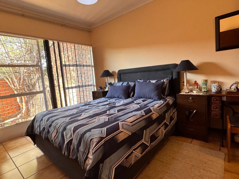 A bedroom featuring tiled flooring and a large window with security bars, providing natural light and a view of the exterior.