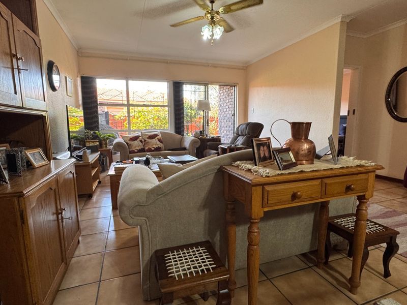 A spacious living room featuring tiled flooring, a ceiling fan, and large sliding glass doors that provide natural light and access to the exterior.