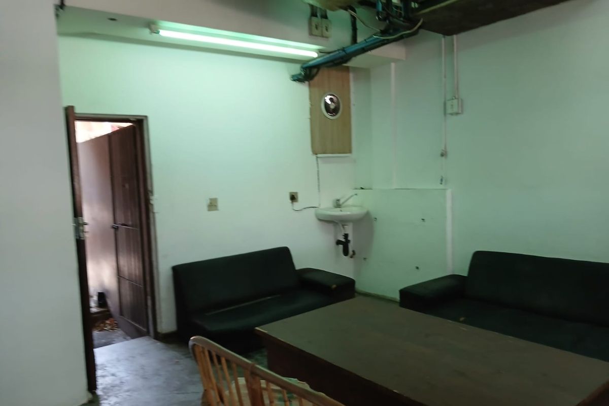 A basic commercial interior space featuring exposed ceiling infrastructure, a wall-mounted basin, and functional lighting, requiring cosmetic updates to improve its overall condition.