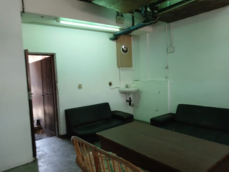 A basic commercial interior space featuring exposed ceiling infrastructure, a wall-mounted basin, and functional lighting, requiring cosmetic updates to improve its overall condition.