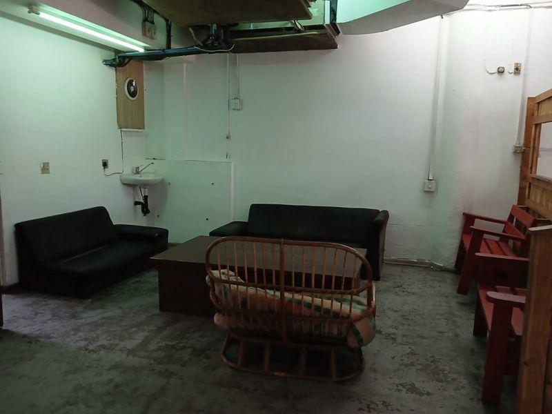 A utilitarian commercial space featuring exposed ceiling infrastructure, concrete flooring, and a wall-mounted basin, suitable for renovation or conversion into a functional office area.