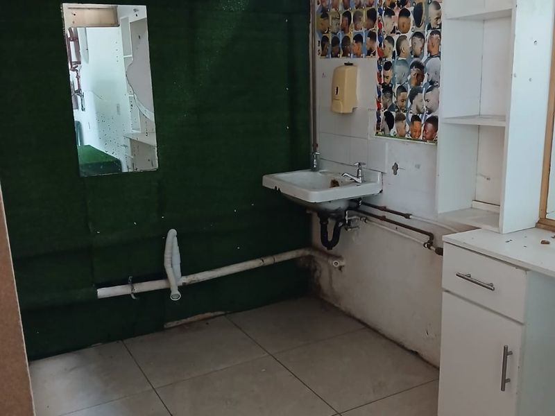 A utility space featuring a wall-mounted basin, exposed plumbing, and built-in cabinetry, currently in need of cosmetic refurbishment and finish repairs.