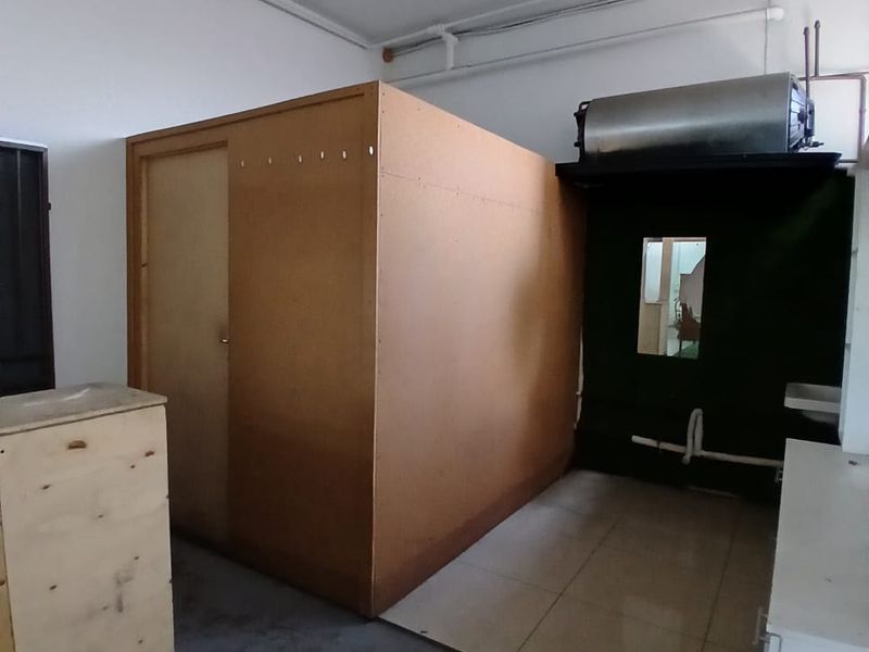 A utility space featuring exposed piping, a water heater, and a partitioned area with tiled flooring, suitable for storage or functional workspace.