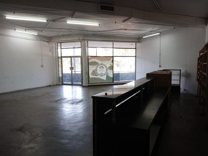 Spacious open-plan commercial unit featuring large storefront windows, exposed ceiling ducting, and a built-in service counter, suitable for retail or office use.