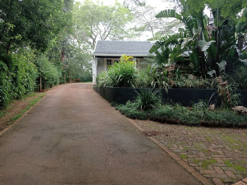 A view of the property entrance featuring an asphalt driveway, brick paved border, and a landscaped retaining wall leading to the main house structure.