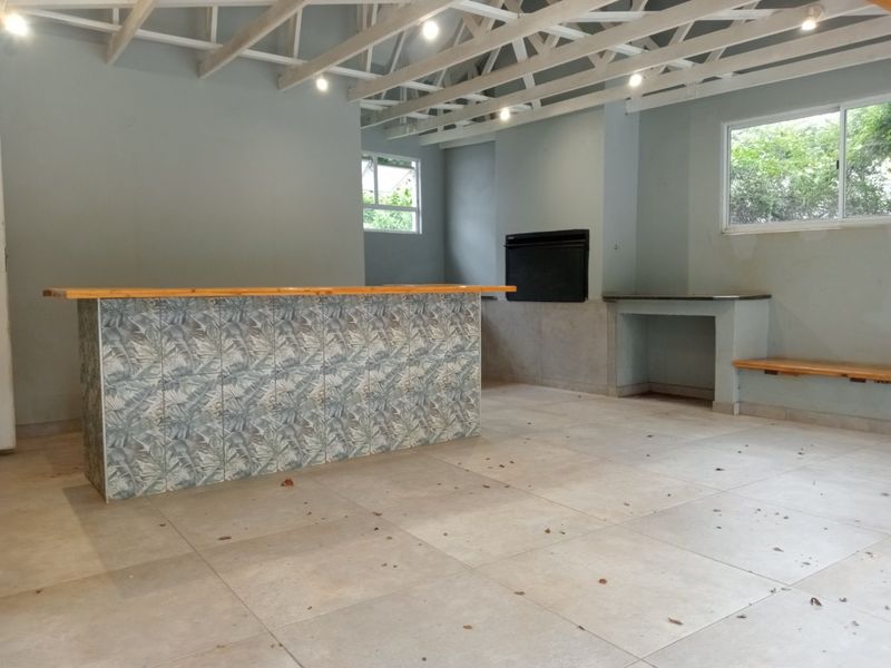 Spacious entertainment area featuring a built-in bar, fireplace, exposed timber roof trusses, and tiled flooring, offering a versatile space for social gatherings.